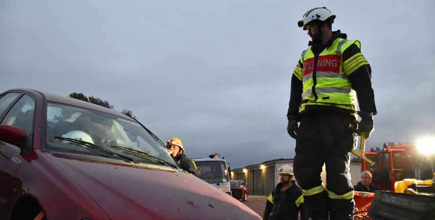 Brandman som står och tittar på en röd bil vid ett övningstillfälle.