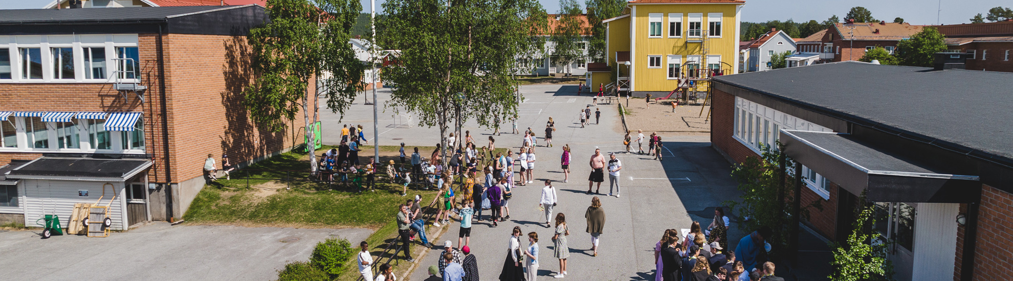 Överblicksbild av Vindelälvsskolans skolgård. Flera finklädda barn och lärare står på skolgården.