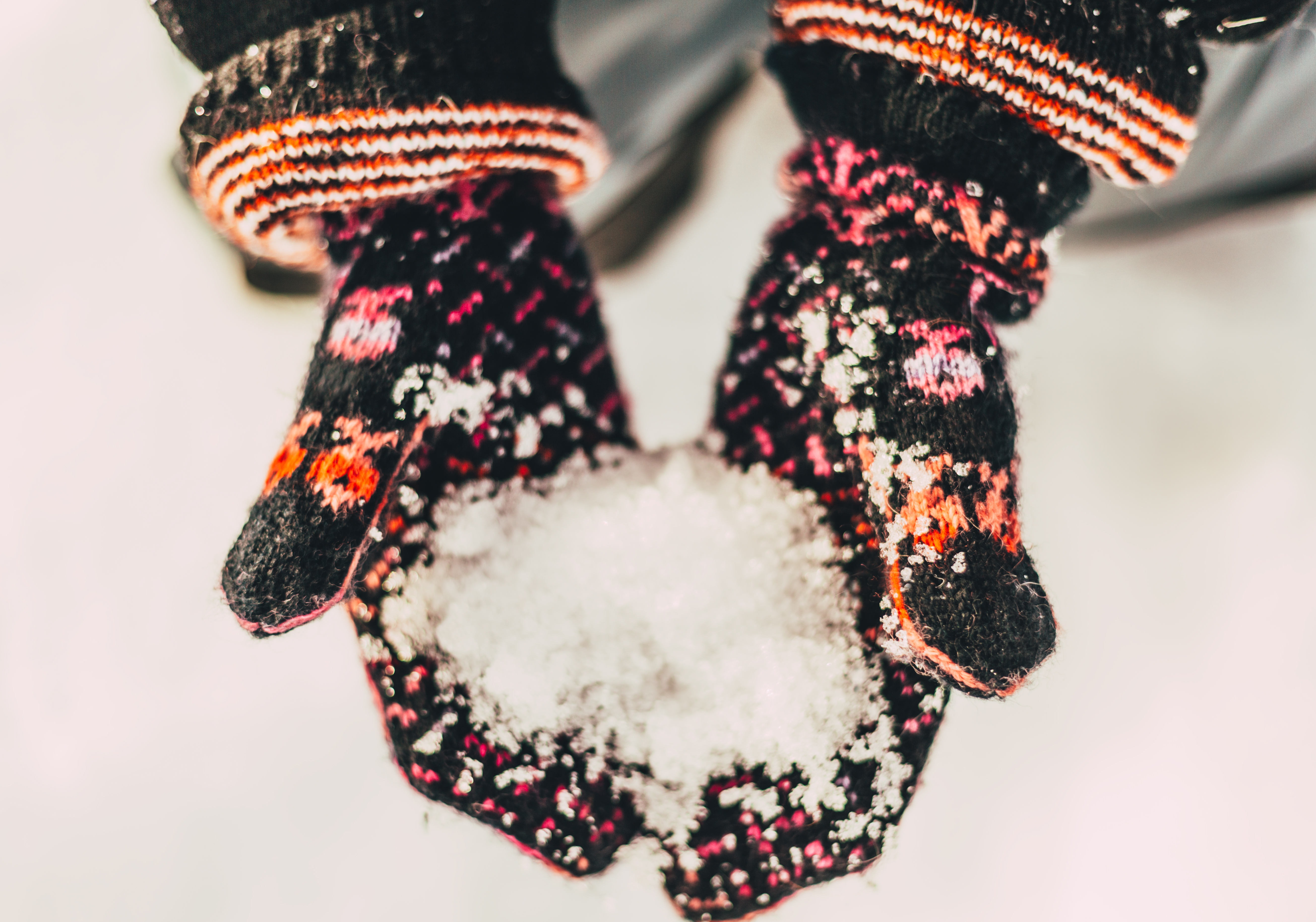 två öppna händer med stickade vantar på som håller i snö