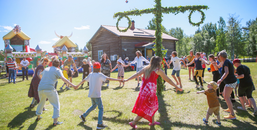 Barn och vuxna som dansar runt midsommarstång